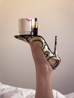 A high heel shoe balancing a coffee cup and lipstick on a bare leg