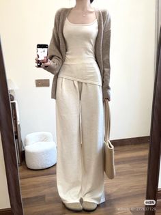 Person in a neutral-colored cardigan and wide-leg pants taking a mirror selfie