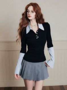 Woman with long red hair and glasses wearing a collared shirt and pleated skirt indoors