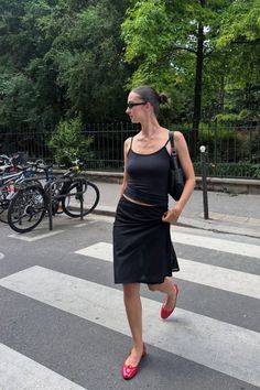 Woman in a black tank top and skirt crossing a street
