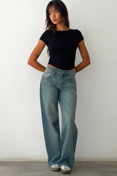 Woman with long hair wearing a black top and loose jeans indoors