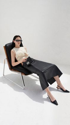Woman with black hair and sunglasses sitting in a chair, wearing a black leather skirt