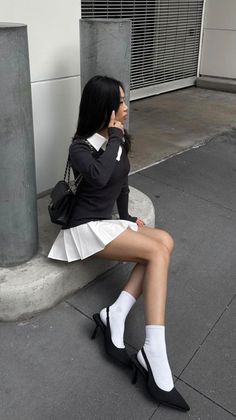 Woman with long black hair wearing a white pleated skirt and black sweater outdoors