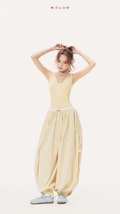 Woman in a yellow top and striped pants with hands raised on a white background