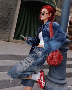 Woman with red hair in a denim jacket and baggy jeans leaning on a pole