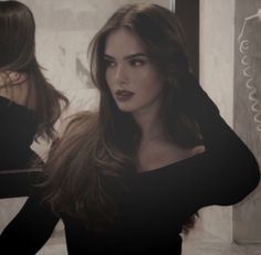 Woman with long dark hair and red lipstick in a black top looking into a mirror