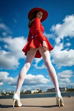 Woman in a red dress and white tights posing outdoors under a blue sky