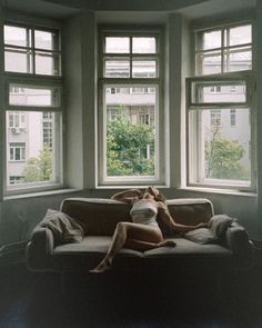 Woman in a white tank top lying on a sofa by a window