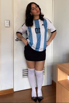 Woman in a soccer jersey, black mini skirt, and white knee socks posing indoors