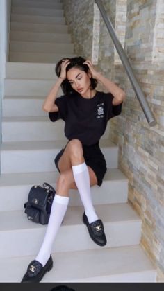 Woman with short black hair sitting on stairs in a black t-shirt and mini skirt