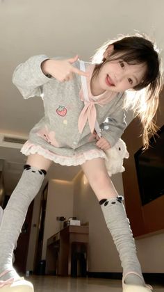 Woman in a grey dress with a pink bow and panda thigh-high socks posing indoors
