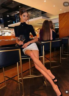 Woman in a black top and white mini skirt sitting at a bar with a drink