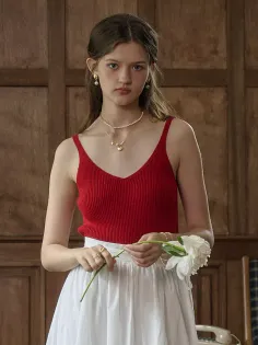 Young woman in a red top and white skirt holding a white flower indoors