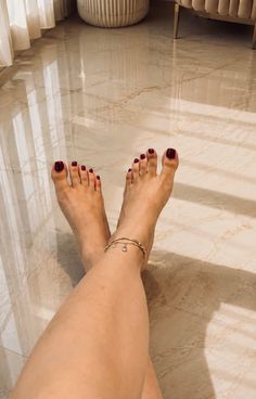Woman's feet with red nail polish and an anklet on a marble floor
