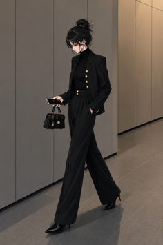 Woman in a black suit and turtleneck holding a phone and handbag indoors