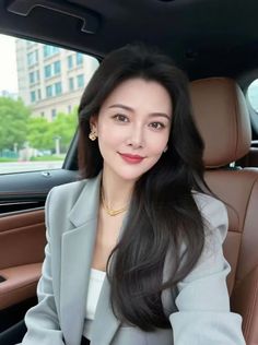 Woman with long dark hair wearing a gray blazer and gold jewelry in a car