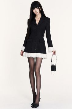 Woman in a black pinstripe dress with lace trim and black tights holding a mini bag
