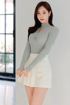 Woman with long dark hair wearing a light green ribbed top and white mini skirt indoors