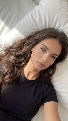 Woman with long wavy hair and green eyes lying on a white bed