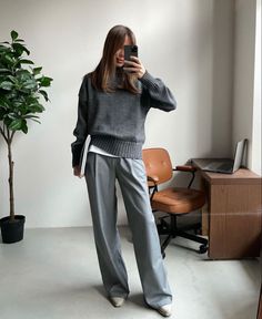 Woman in a gray sweater and wide leg pants taking a mirror selfie indoors