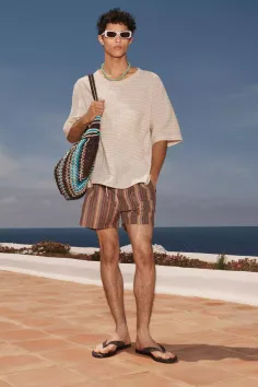 Man in striped shorts and a t-shirt holding a crochet bag outdoors