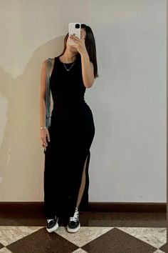 Woman in a black dress and sneakers taking a mirror selfie