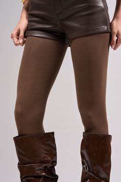 Person wearing brown shorts, tights, and boots in a studio setting