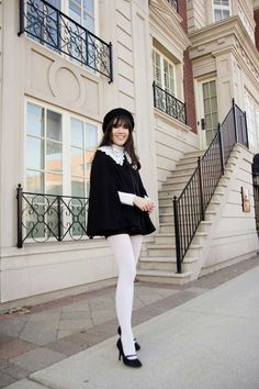 Woman in a black cape and white tights standing outdoors