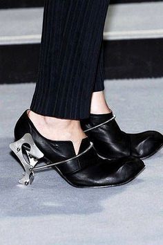 Close up of black shoes with unique metal heels and pleated pants