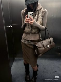 Person in a fur vest and midi skirt taking a mirror selfie indoors