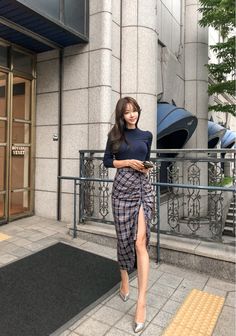 Woman in a plaid skirt with a high slit and a dark top on a city street