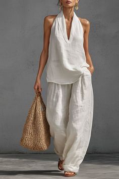 Woman in a white linen halter top and wide leg pants holding a straw bag
