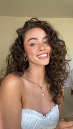 Woman with curly hair and gold jewelry smiling in a white top