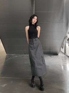 Woman with black hair wearing a black top and cargo skirt with platform shoes