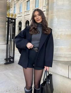 Woman in a black coat and shorts with tights standing outdoors
