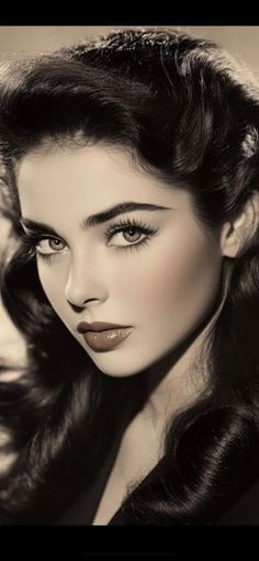 Woman with dark wavy hair and striking makeup in a black and white portrait