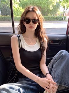 Woman with long hair and sunglasses in a car, wearing a layered top and jeans