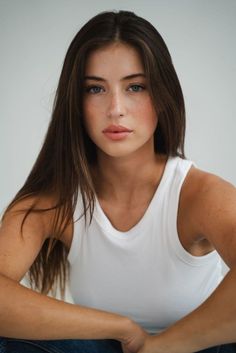 Woman with long brown hair and blue eyes wearing a white tank top