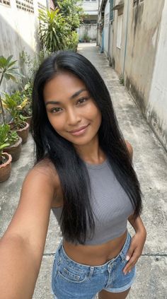 Woman with long black hair in a crop top and denim shorts in an alleyway