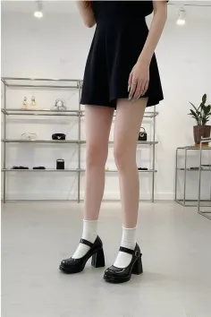 Woman in a black dress and mary jane shoes with white socks indoors