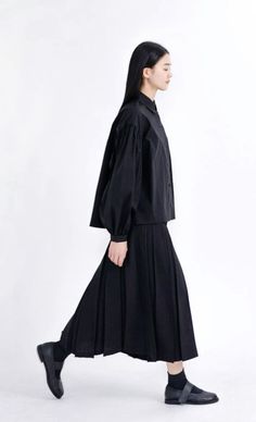 Woman in a black shirt and pleated skirt walking against a white background