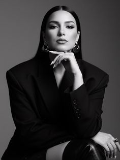 Woman in a black blazer and hoop earrings posing with her hand on her chin