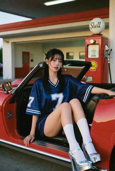 Woman in a blue football jersey and silver platform heels sitting in a red convertible
