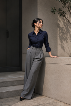 Woman in a navy blue shirt and grey wide leg pants leaning against a wall