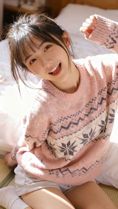 Woman in a pink sweater and shorts smiling indoors with soft lighting