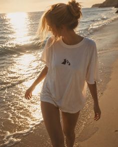 Woman in a white t-shirt walking on a beach at golden hour