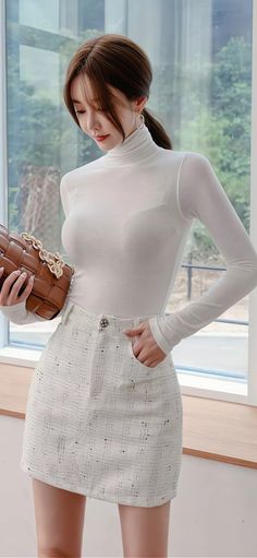 Woman in a white turtleneck and mini skirt holding a brown handbag indoors