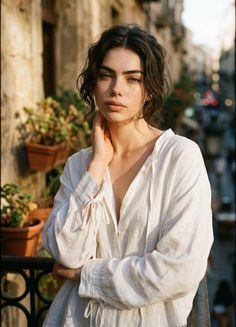 Woman with curly hair and freckles in a white shirt on a balcony