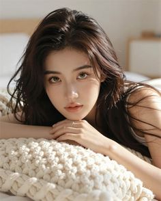 Woman with long dark hair lying on a bed with a knitted blanket