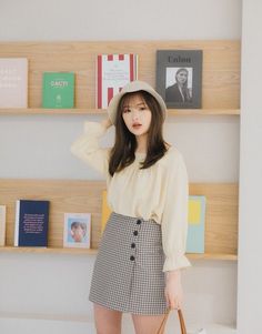 Woman in a bucket hat and gingham skirt standing in front of a bookshelf